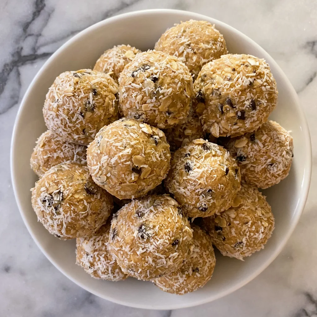 A bowl of energy balls made with oats, shredded coconut, and chocolate chips, displayed on a marble surface