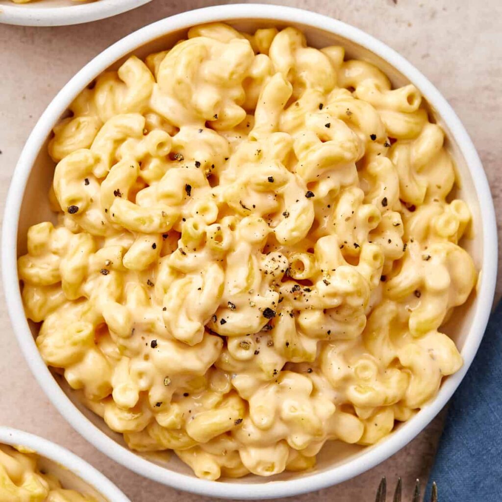 Close-up of a creamy stovetop mac and cheese served in a white bowl, topped with freshly cracked black pepper.