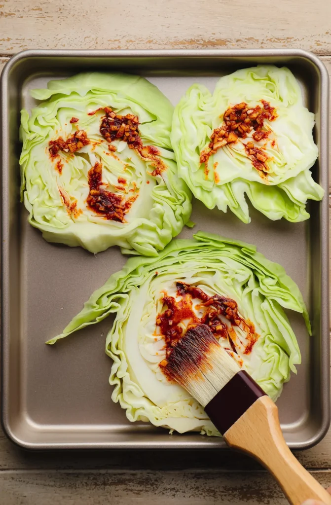 A plate of roasted cabbage steaks topped with golden breadcrumbs, fresh parsley, and a hint of garlic, served with a fork on a dark marble table.