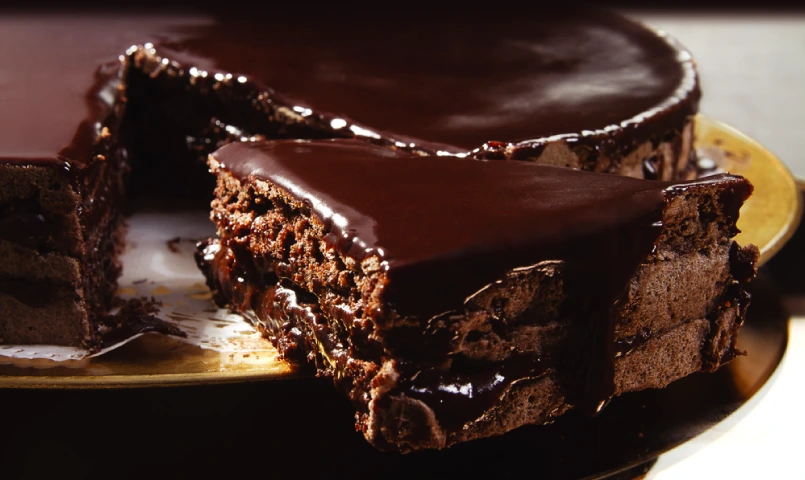 A decadent chocolate layer cake with rich chocolate ganache coating, partially sliced to reveal the moist layers filled with creamy chocolate frosting.