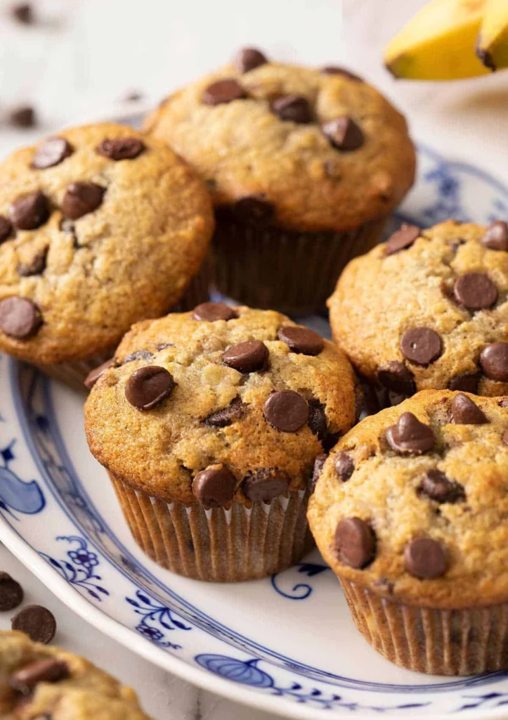 Freshly baked banana chocolate chip muffins on a decorative blue and white plate, topped with melted chocolate chips.