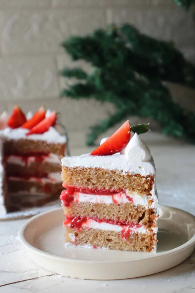 A slice of eggless strawberry shortcake with layers of fluffy vanilla cake, fresh strawberry filling, and whipped cream, garnished with a sliced strawberry on top.